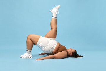 Young overweight woman training in sportswear against blue studio background. Trying hard to lose...