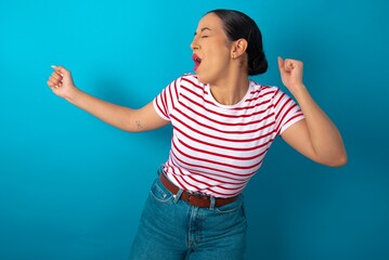 beautiful woman wearing striped T-shirt over blue studio background , dancing and listening music with headphones.