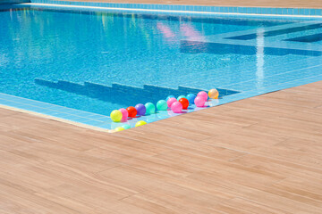 Swimming pool with colorful ball floating water in sunshine day.