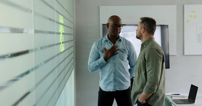 Two diverse businessmen standing in an office boardroom and brainstorming using adhesive notes on a glass wall