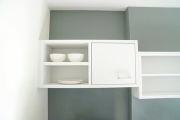 White Cabinet set with dish and bowl setup on gray color wall in modern and minimal style. Design and interior for room in condominium or apartment.