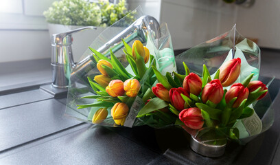 Bouquets of fresh yellow and pink tulips with green stems in a modern black kitchen sink.