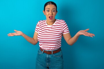 So what? Portrait of arrogant beautiful woman wearing striped T-shirt over blue studio background...