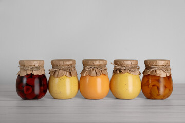 Jars with preserved fruit jams on white wooden table