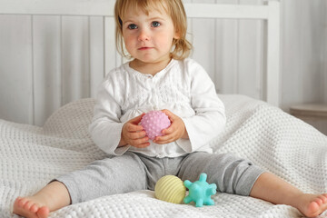 Cute baby girl playing tactile knobby balls. Young child hand plays sensory massage ball. Enhance...