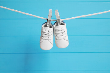 Cute baby shoes drying on washing line against light blue wooden wall