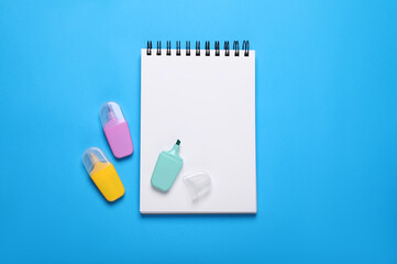 Open notebook and colorful markers on light blue background, flat lay