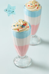 Two Patriotic layered milkshake or sweet dessert for child for Independence Day on blue background. Food for 4th of July or Memorial Day.