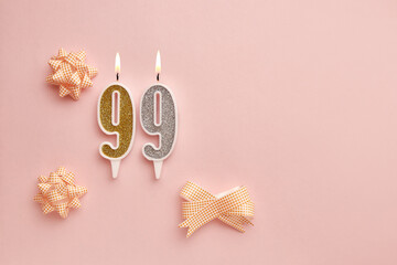 Candles with number 99 on pastel pink background with festive decor. Happy birthday candles. The concept of celebrating a birthday, anniversary, important date, holiday. Copy space. banner