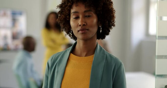 Confident young businesswoman standing at the door of an office boardroom with a group of colleagues meeting in the background