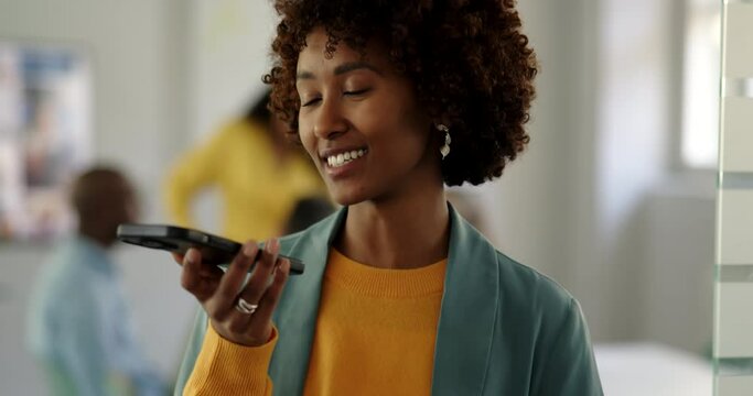 Young businesswoman talking on over her phone's speaker at the entrance of an office boardroom with colleagues meeting in the background