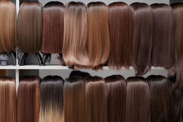 Showcase of natural looking wigs in different shades of brunette fixed on the wig holders in beauty salon. Row of mannequin heads with variation colors hair on shelf in wig shop - obrazy, fototapety, plakaty