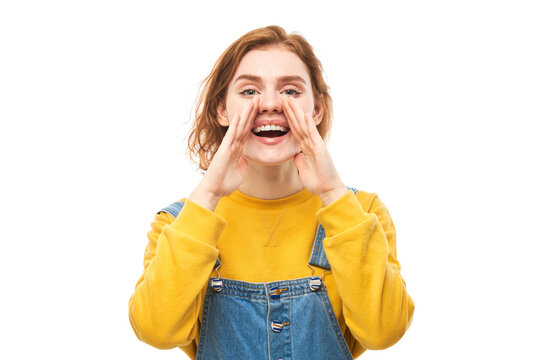 Portrait of redhead young woman screaming into her palms on white studio background. Important information, news concept