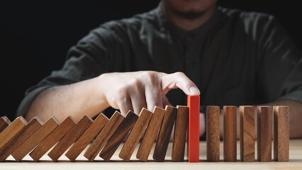 Businessman hand stopping wooden domino business crisis effect or risk protection on dark...