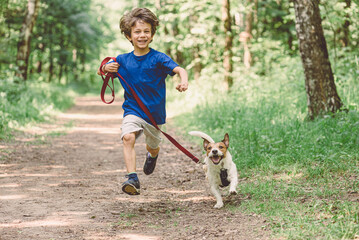 Happy boy running with dog on leash by park alley on summer day - Powered by Adobe