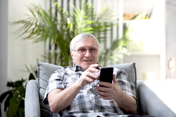 Portrait of aged man sitting on the armchair and talking on phone with his relatives	