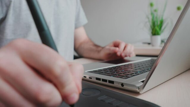 Man takes stylus from drawing tablet and begins to draw. Hand close-up. Tracking left shot. Concept of retouching and digital illustrations.