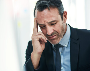 Dealing with a painful and distracting headache. a mature businessman looking stressed out while working on a computer in an office.