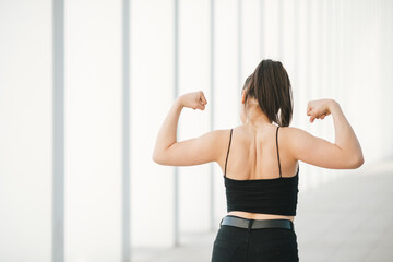 Girl with black raised hair shows back and muscles on white background