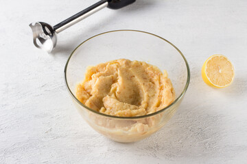 Glass bowl with pureed quince, immersion blender and half a lemon on a light gray background. Stage of preparation of vegan quince pastille or other dessert