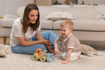 Happy family at home. Mother and baby boy playing with toys at home indoors. Little toddler child and babysitter nanny having fun together. Young woman mom kid son rest in living room - obrazy, fototapety, plakaty