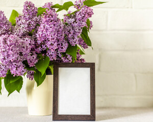 Empty wooden photo frame and lilac bouquet on table with copy space.