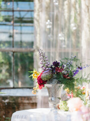 Bouquet of artichoke, delphinium, anthurium, iris in a silver vase. Greenhouse wedding decor.