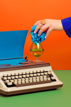 Crop woman with typewriter putting crumpled paper into glass cup