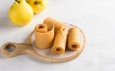 Natural quince pastille on a wooden board surrounded by fresh quince fruits on a light gray background