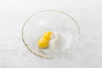 Glass bowl with sugar and two yolks on a light gray background. Dough kneading for homemade cookies