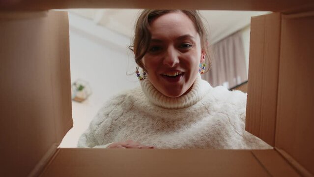 Inside view from box. Young happy woman unpacking delivery parcel at home. Smiling satisfied girl shopper, online shop customer opening cardboard receiving purchase gift by fast postal shipping order