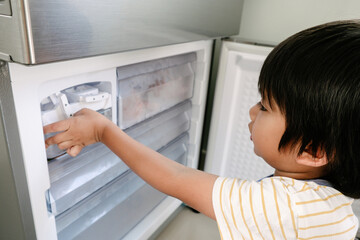 Little boy trying to get some ice from the ice maker in the refrigerator