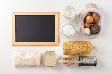 food storage and eating concept - close up of different cereals, groceries and preserves and chalkboard on white background, top view