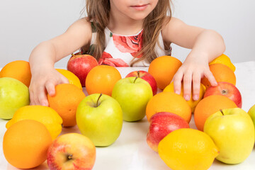 Fototapeta na wymiar the child's hands lie on a variety of fruits on the table, apples, lemons, oranges