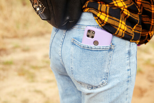 Woman puts mobile phone in jeans pocket on yellow nature background. Blue denim. Smart phone in the purple case. Out of focus