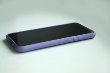 Smartphone in purple plastic case on white background, gloomy day. Black screen. Mockup, mock-up, mock up. Nobody. Smart phone. Out of focus