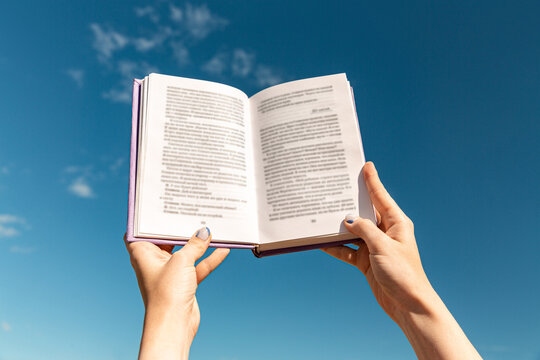 reading, education and knowledge concept - close up of hands holding open book over blue sky