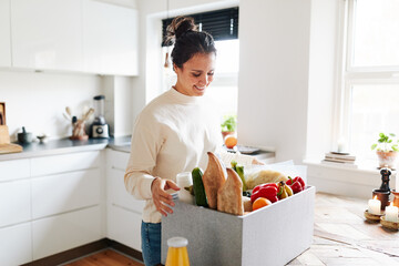 Smiling woman unpacking groceries in her kitchen