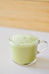 Matcha latte with oatmilk in a glass mug or cup with a neutral and blurry background. Matcha latte is yellow or green in color and has foamy and frothy oatmilk.