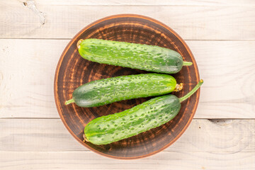 Three ripe green cucumbers with a clay plate on a wooden table, macro, top view.