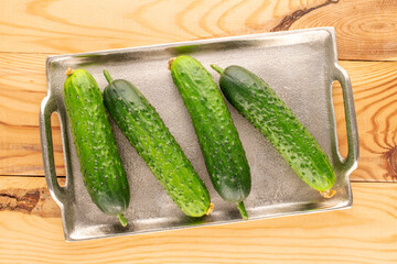 Four ripe green cucumbers with a metal tray on a wooden table, macro, top view.