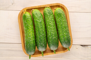 Four ripe green cucumbers with bamboo plate on wooden table, macro, top view.