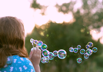 girl blowing soap bubbles, abstract blurred natural background. rear view. dreaming, harmony...