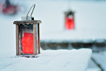 Rustic wooden lanterns on tables outside, red candles inside the lanterns. Tables are covered in...