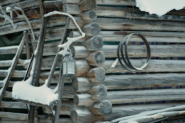 Old rustic houses made of timber and covered in snow. Some tools on the side of the wooden house. Snowy village in Lapland, Finland on a cold winter day.