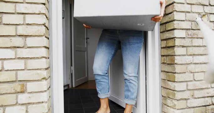 Woman in a protective face mask bringing a delivery box full of groceries into her home from her doorstep