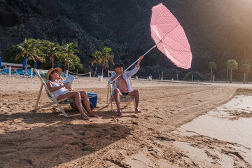 Senior couple placing the umbrella that had been blown away by the wind. Concept: beach day,...
