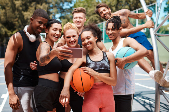 Gather around for a team selfie. a group of sporty young people taking selfies together on a sports court.