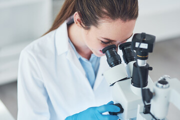 Seeing life at a small scale. a focused young female scientist looking through a microscope while...