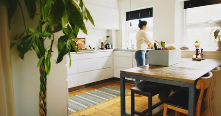 Young woman standing at a table in her kitchen unpacking a box of delivered groceries - Powered by Adobe